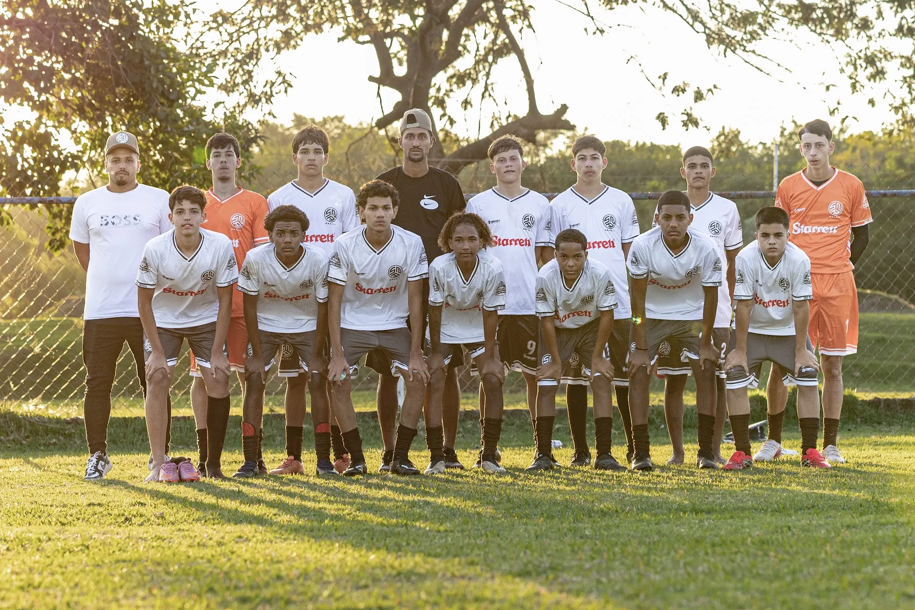 Atletas e comissão técnica da SNA Brasil, de uniforme branco, perfilados no gramado
