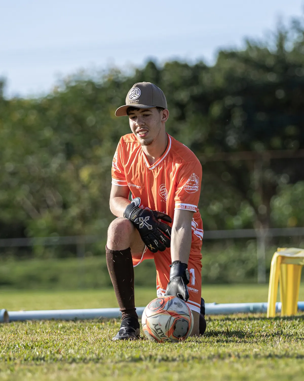 Goleiro de camisa laranja agachado com a bola